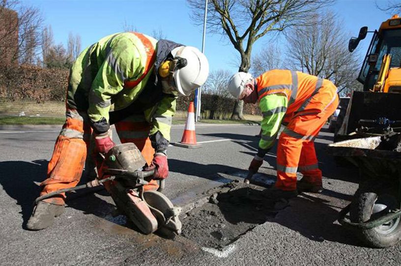 Construction worker cutting up pavement on a roadway.